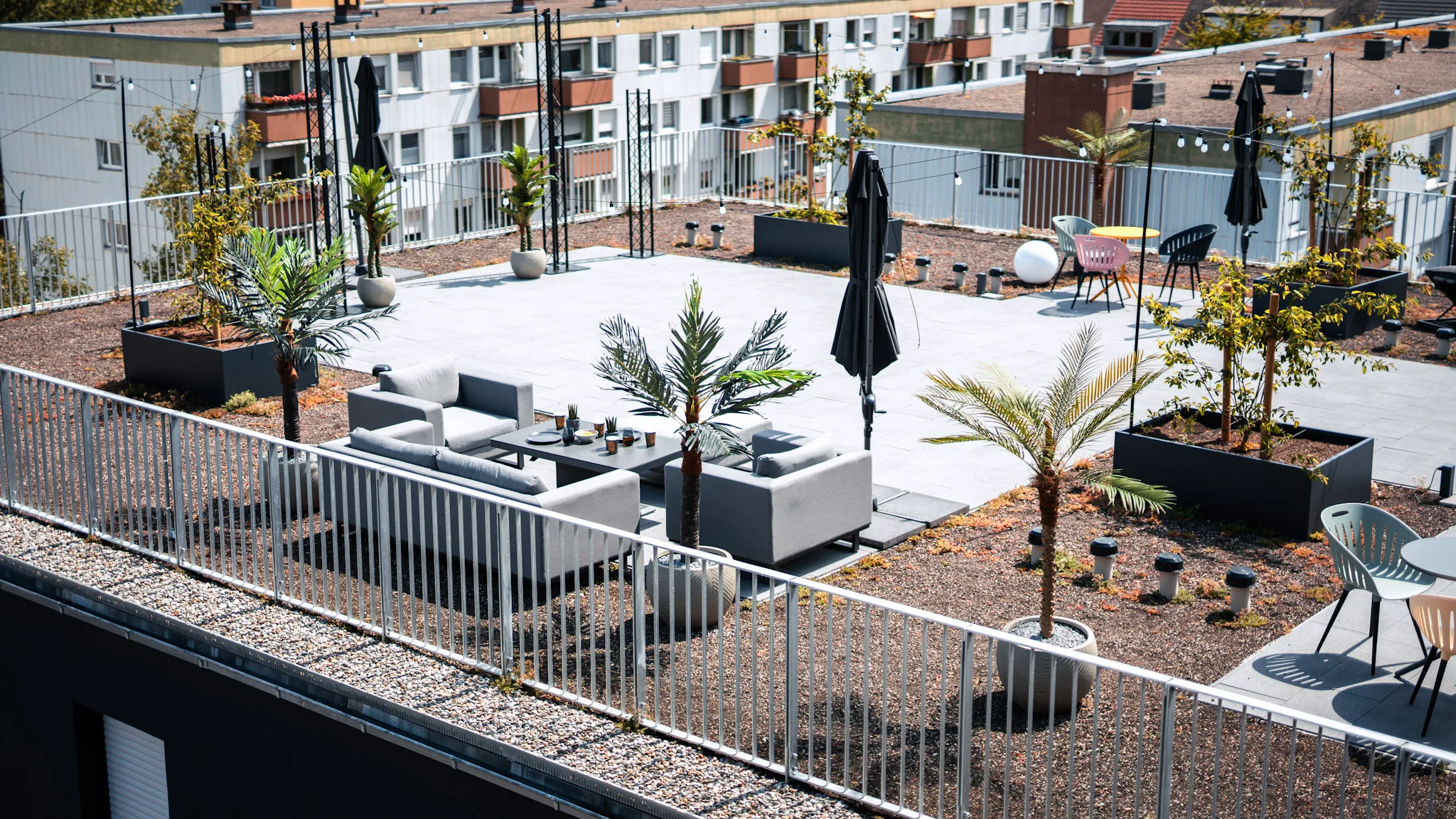 Rooftop-Terrasse der Eighty-Eight Apartments Nürnberg bei Tag mit Loungemöbeln und Palmen